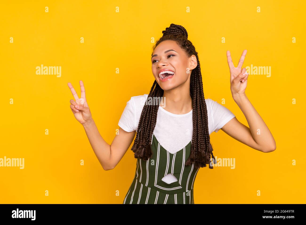 Ritratto di attraente ragazza allegra che mostra doppio segno a V avendo divertimento isolato su sfondo giallo luminoso Foto Stock