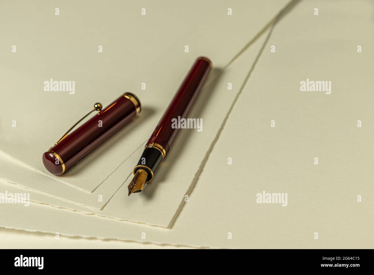 Penna stilografica rosso scuro con pennino d'oro e cappuccio sciolto su una serie di fogli di carta color crema come foto di sfondo Foto Stock