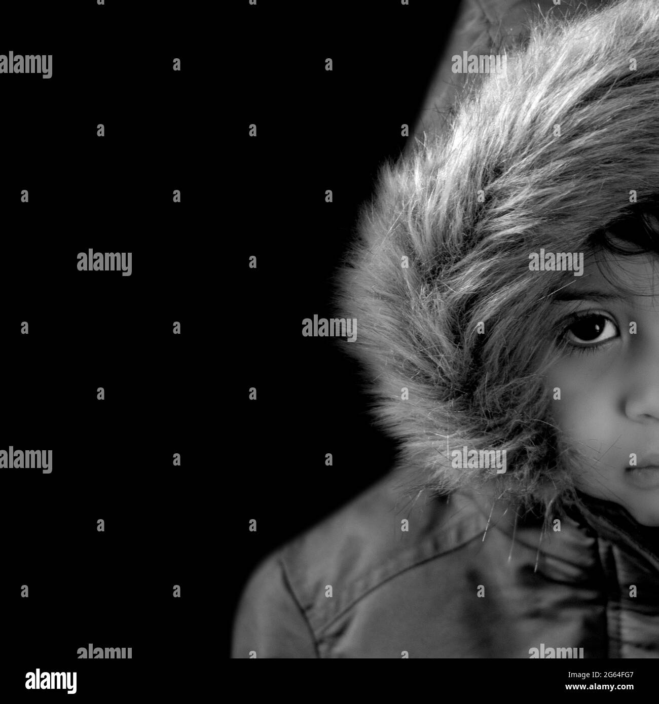 medio primo piano ritratto bambino con un parka in pelliccia cappuccio monocromatico con uno sguardo timido. copia spazio, sfondo nero Foto Stock