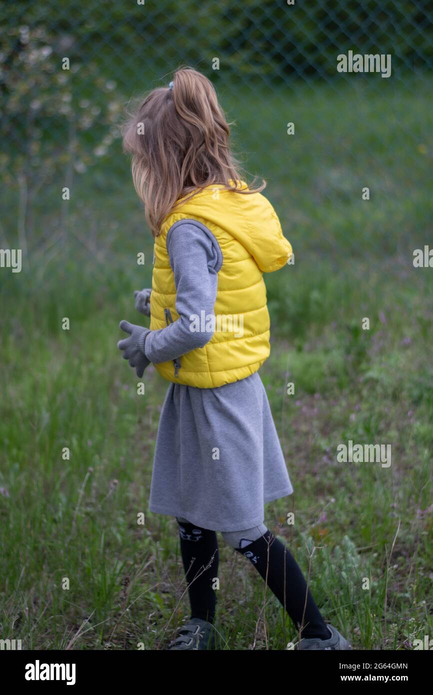 Ragazzina che cammina in erba sul cortile e indossa abiti di colore trendy dell'anno 2021 - giallo illuminante e grigio estremo Foto Stock