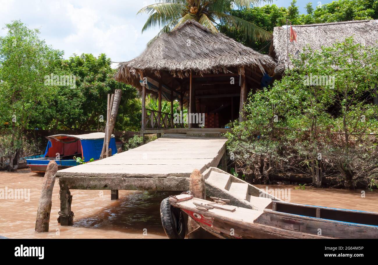 Molo e casa di paglia sul delta del Mekong in Vietnam con una barca di pesca in legno ancorata. Foto Stock