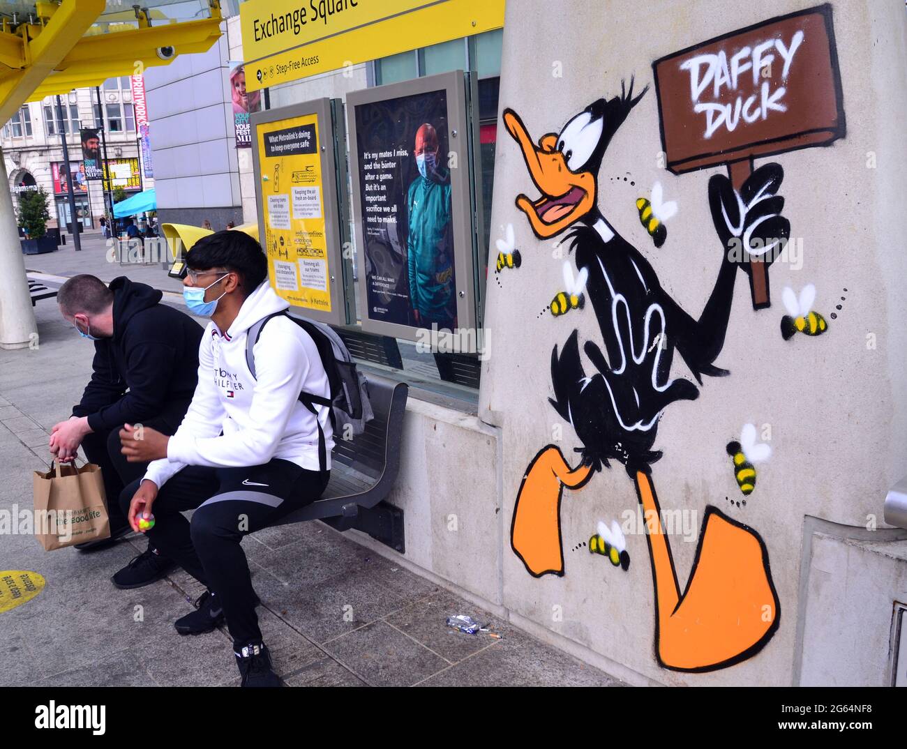 Gli uomini siedono accanto a un'immagine del personaggio dei cartoni animati di Daffy Duck, parte di un percorso artistico Looney Tunes che ha aperto a Manchester, in Inghilterra. Foto Stock