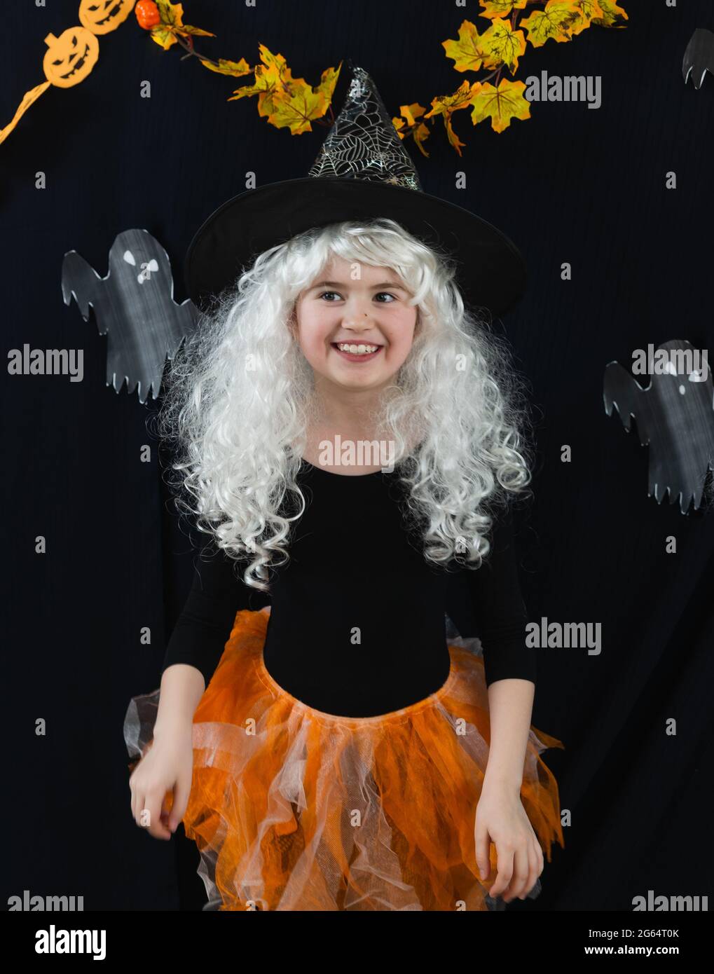 Una ragazza allegra in una parrucca bianca e un costume di strega su uno sfondo nero con fantasmi. Orrore divertente Foto Stock