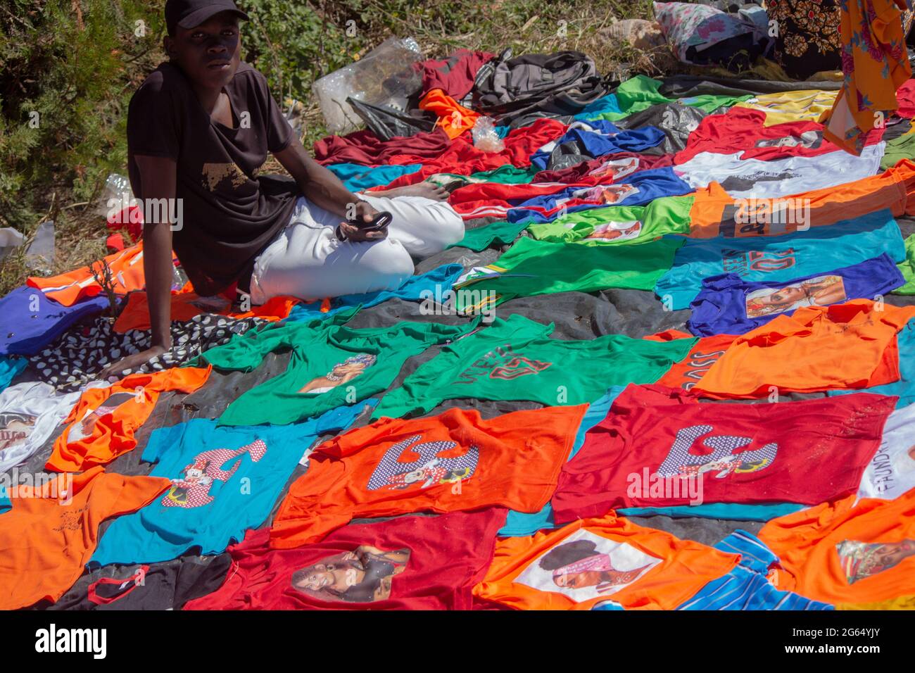 Venditore di strada che vende la varietà di t-shirt stampate su uno stand di terra Foto Stock