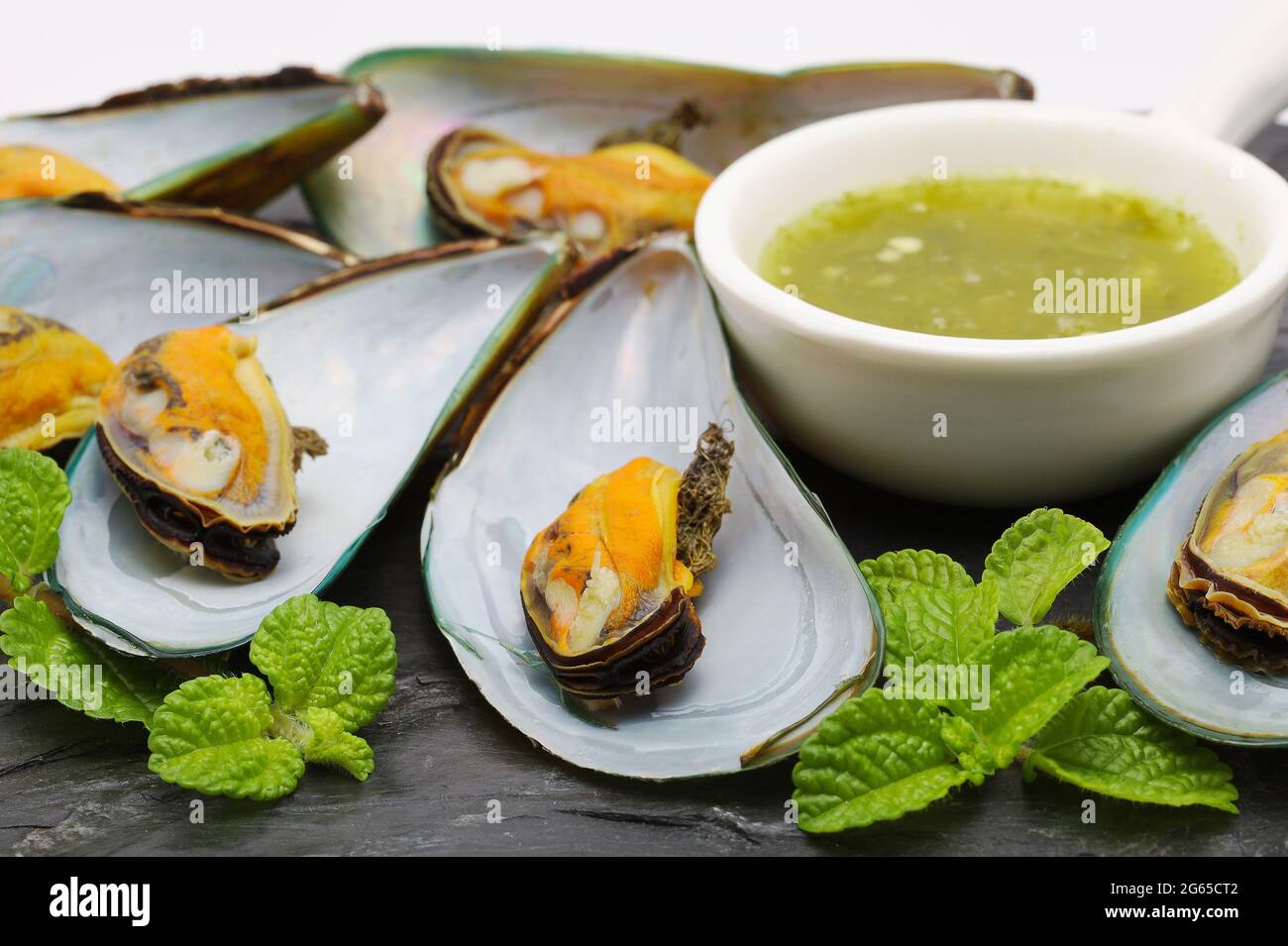 Le cozze con salsa piccante sono poste su uno sfondo di pietra nera. Foto Stock