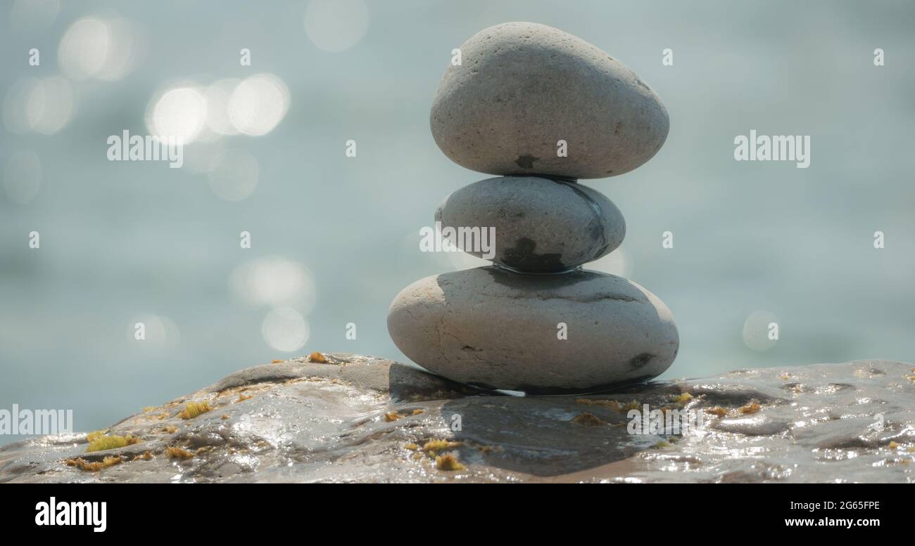Equilibrata piramide di ciottoli sulla spiaggia in una giornata di sole. Abstract Sea bokeh sullo sfondo. Messa a fuoco selettiva. Pietre Zen sulla spiaggia di mare, meditazione Foto Stock