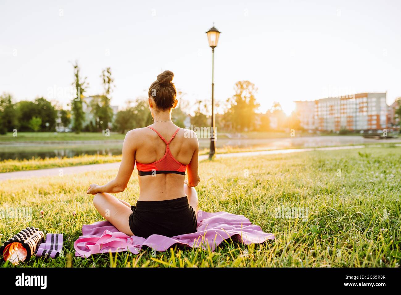 Donna che indossa abbigliamento sportivo che pratica yoga nel parco. La donna siede in posizione di loto e medita durante l'alba. Foto Stock