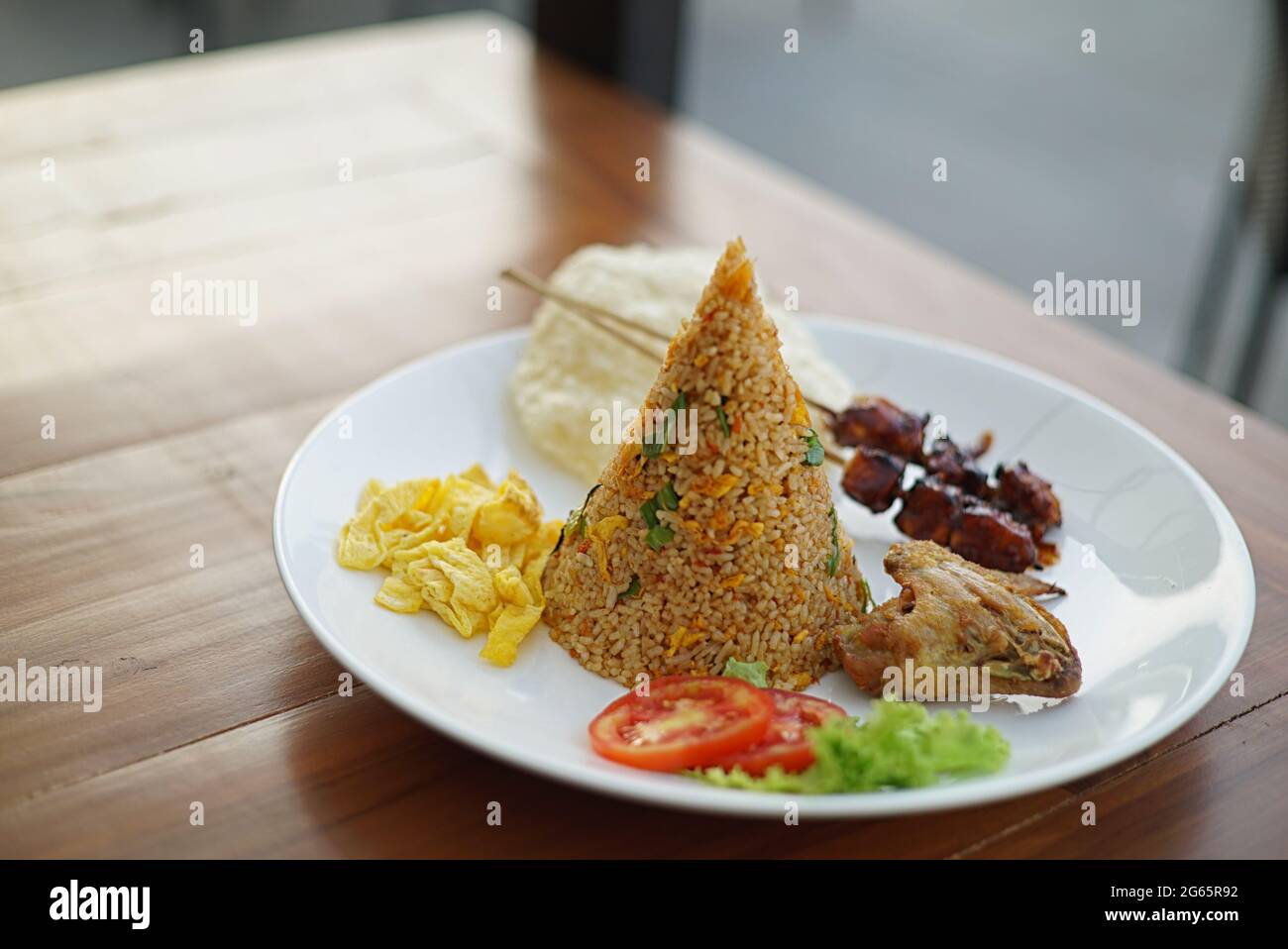 Riso fritto tradizionale in piatto con uova strapazzate, satay di pollo, pollo fritto e cracker di riso Foto Stock