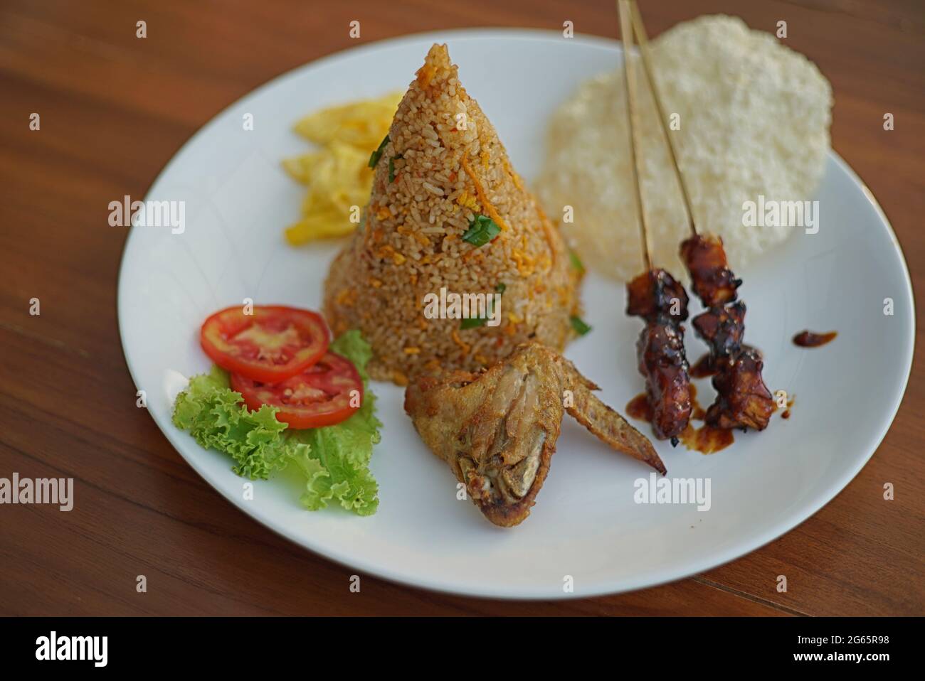 Riso fritto tradizionale in piatto con uova strapazzate, satay di pollo, pollo fritto e cracker di riso Foto Stock