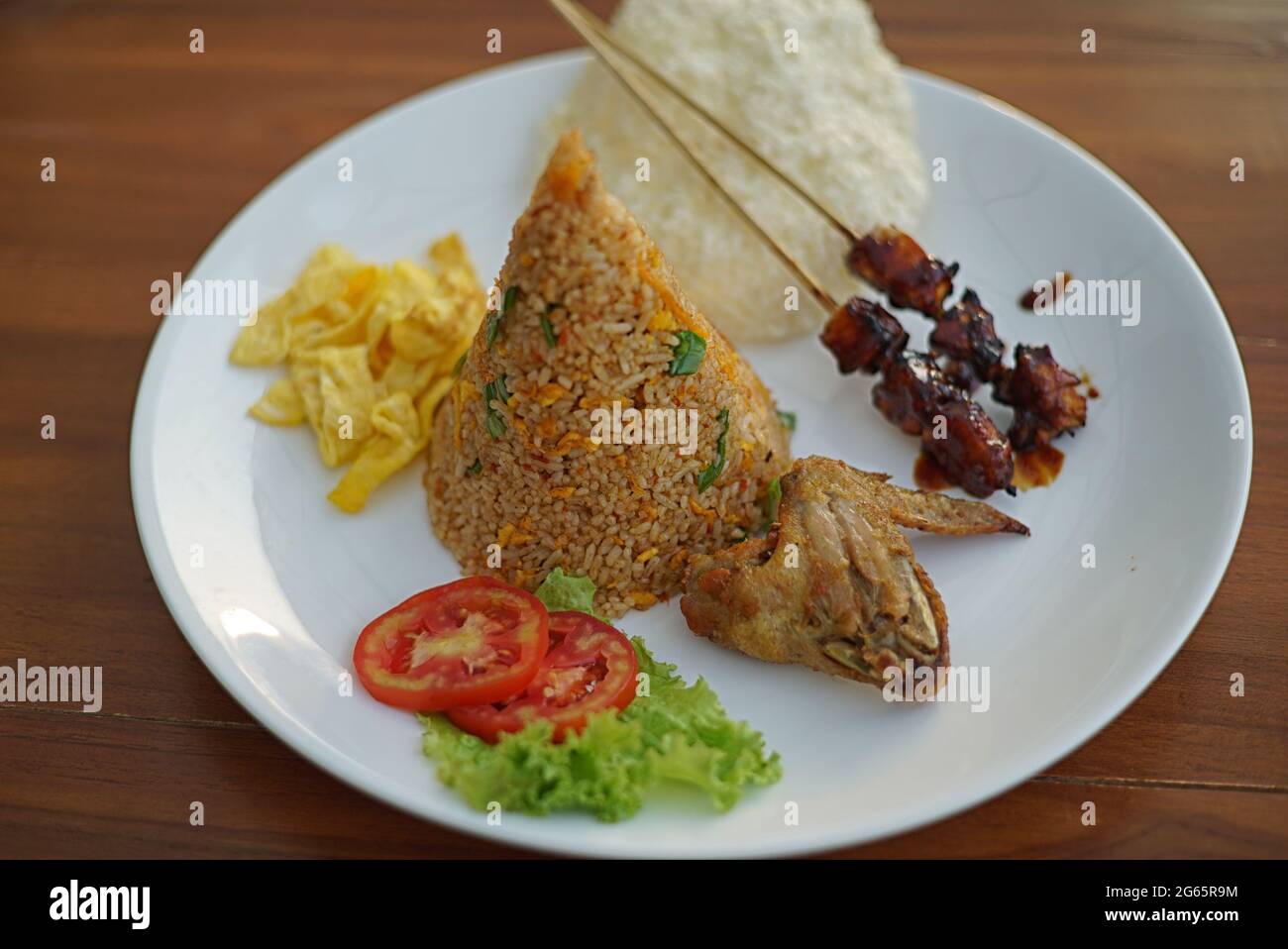 Riso fritto tradizionale in piatto con uova strapazzate, satay di pollo, pollo fritto e cracker di riso Foto Stock