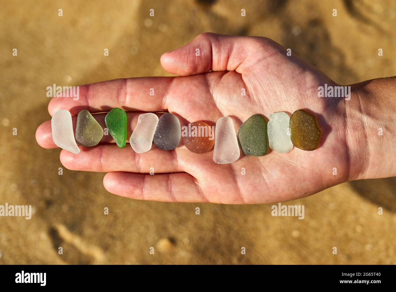 Diversi colori di vetro marino raccolti da una spiaggia sono disposti in una linea sulla mano di una persona Foto Stock