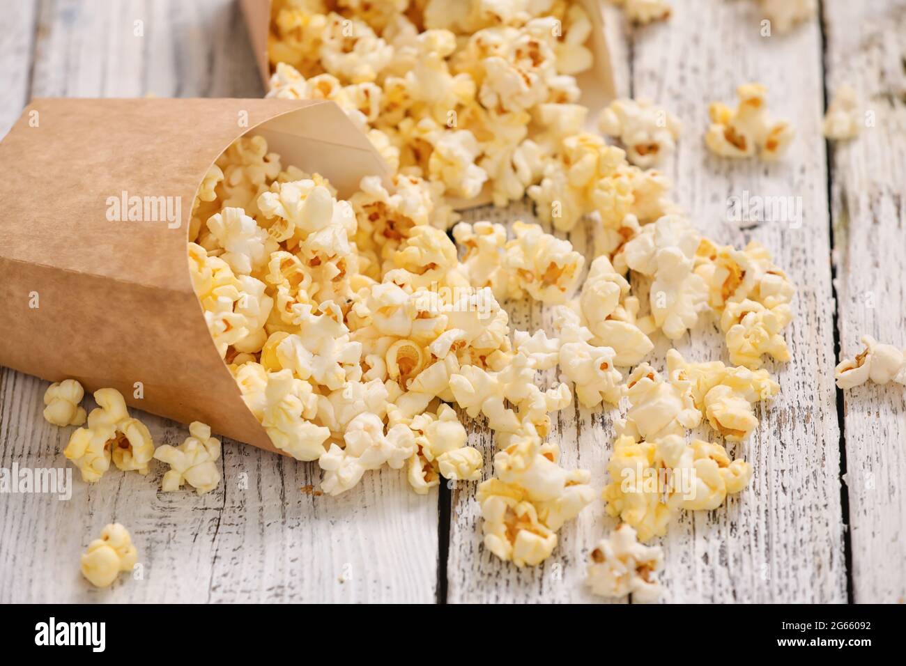 Sacchetti di carta con gustosi popcorn su sfondo di legno chiaro Foto Stock