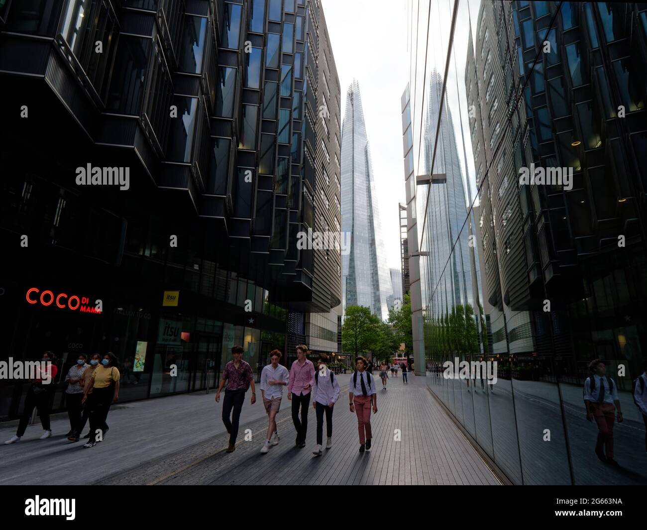 Londra, Greater London, England - Giugno 26 2021: Gli adolescenti alla moda camminano lungo più London Riverside. Il grattacielo Shard si riflette negli edifici. Foto Stock