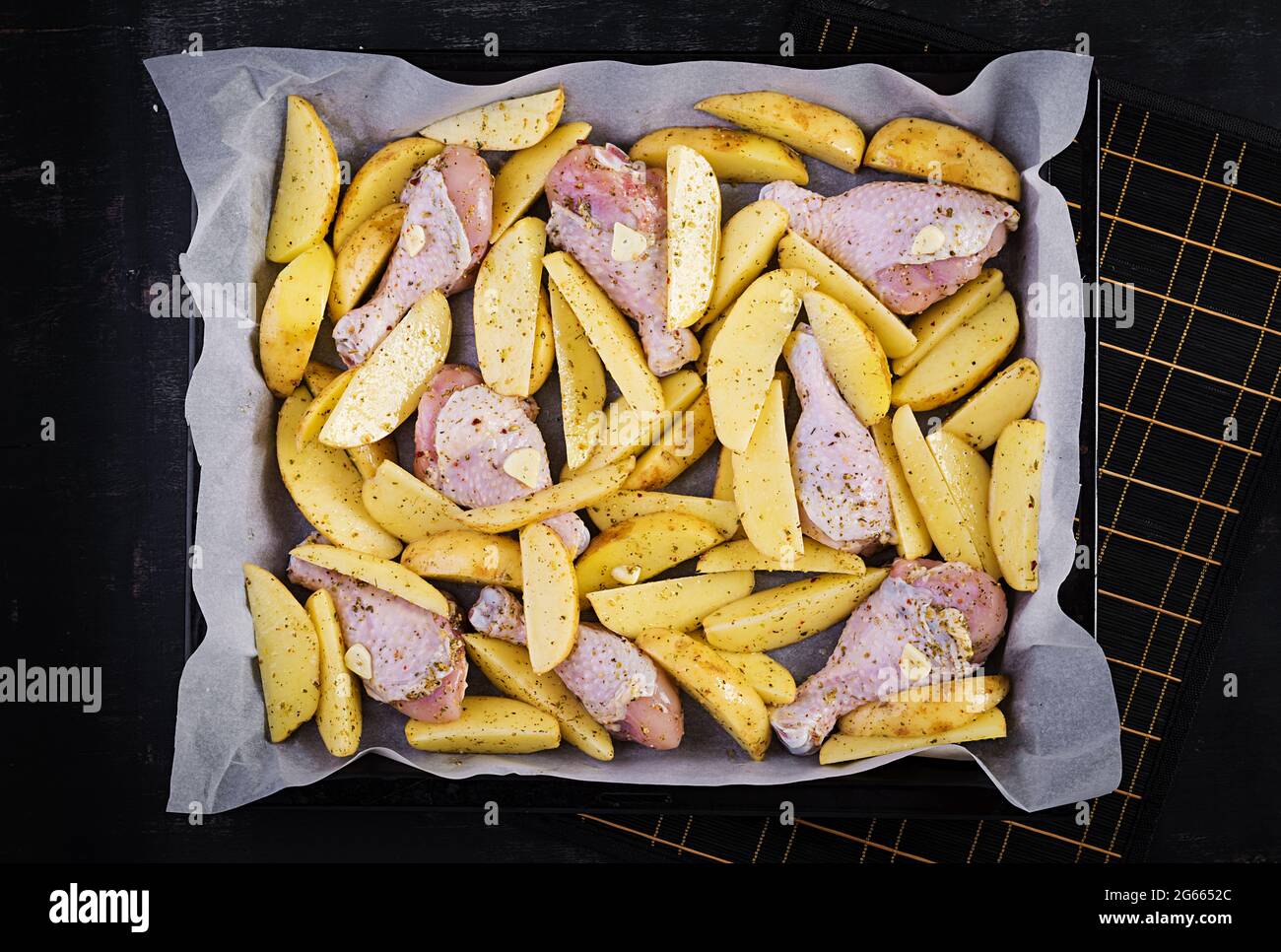 Briciole di pollo crude e spicchi di patate in spezie su una teglia da forno preparata per la cottura. Vista dall'alto, disposizione piatta Foto Stock