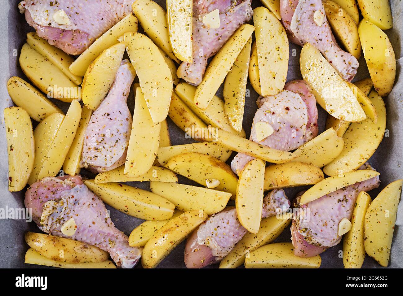 Briciole di pollo crude e spicchi di patate in spezie su una teglia da forno preparata per la cottura. Vista dall'alto, texture Foto Stock