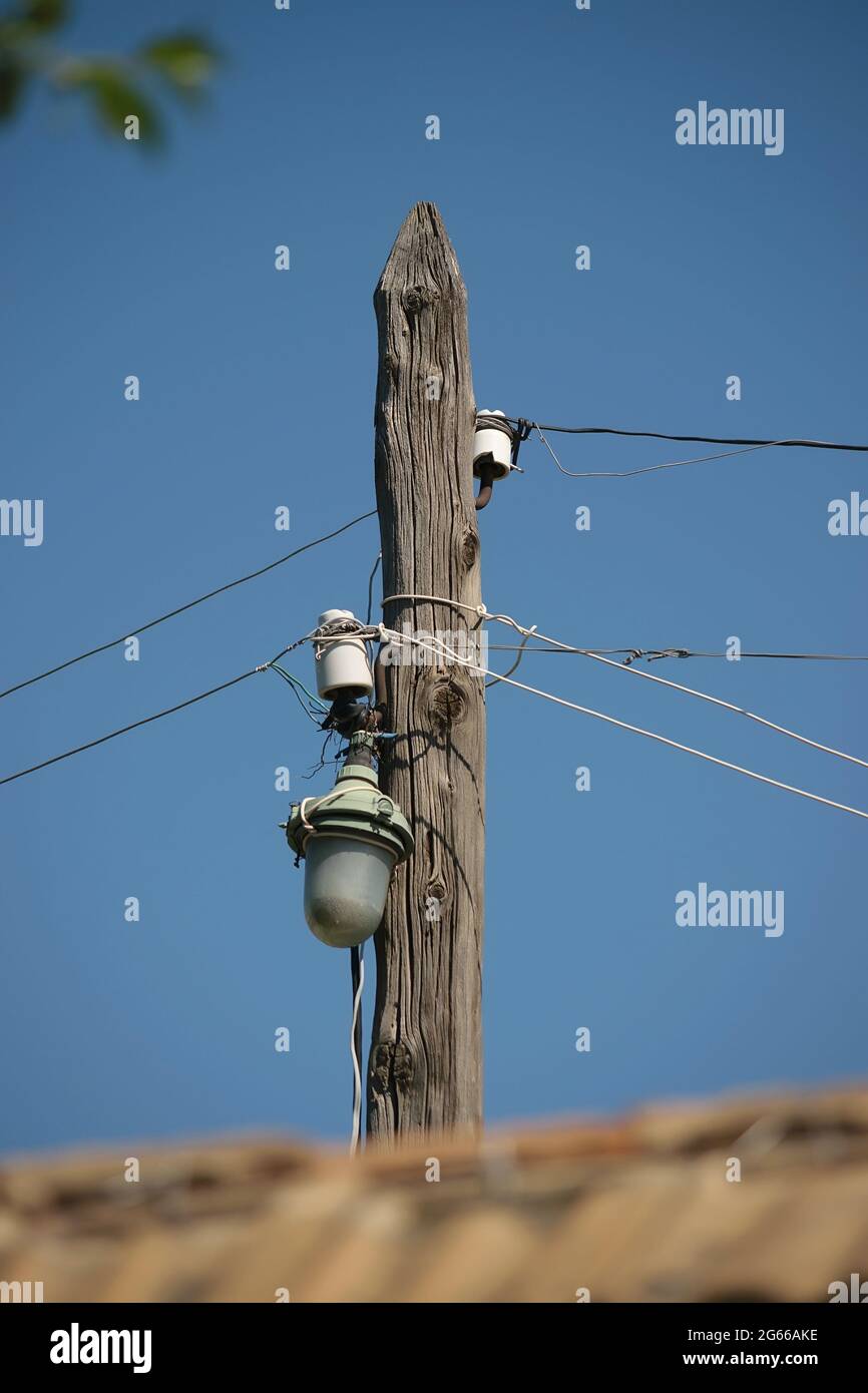 Linee elettriche su un vecchio palo di legno con illuminazione stradale contro il cielo blu nel giorno Foto Stock