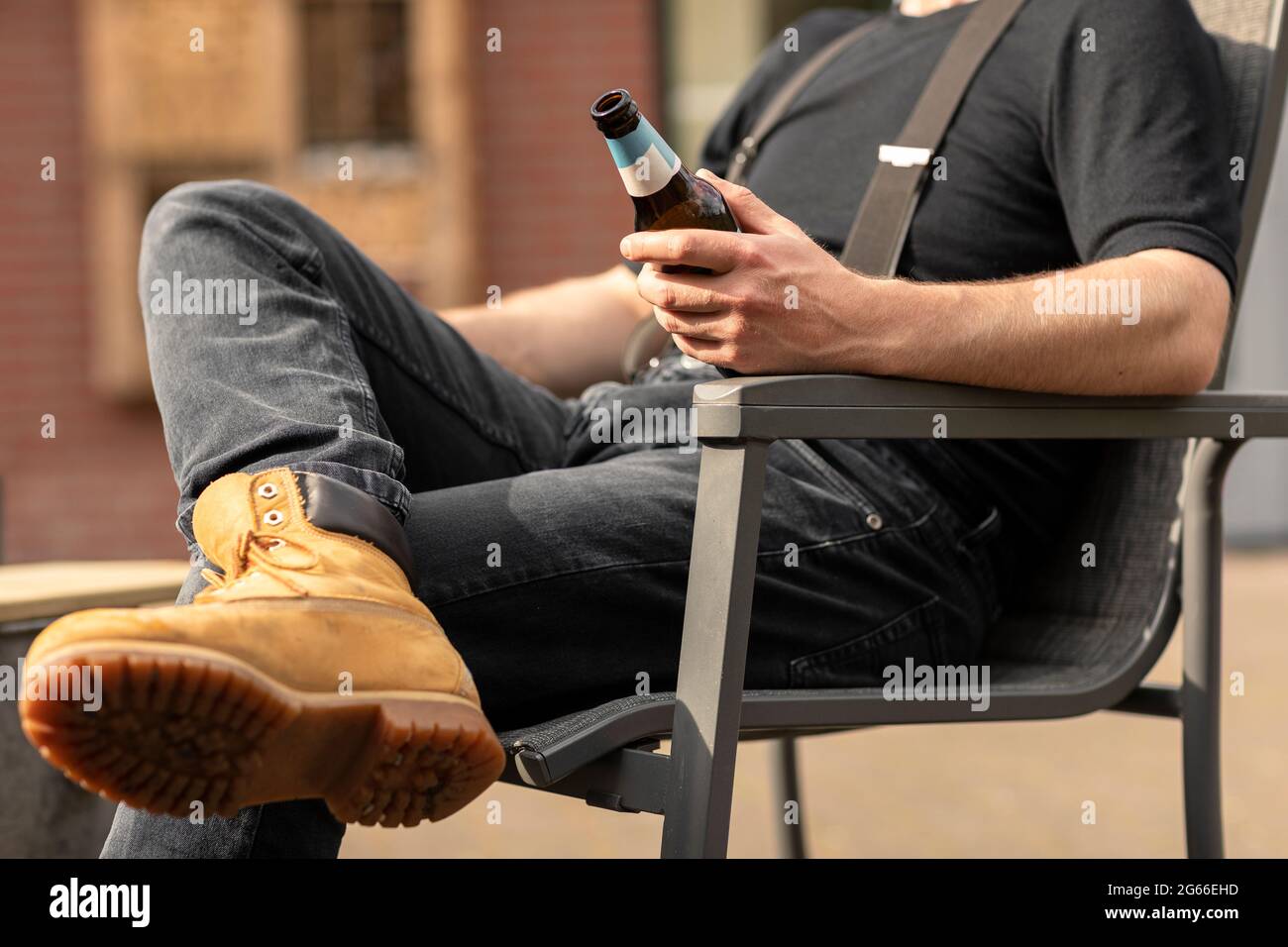 Un uomo che tiene una bottiglia di birra mentre si siede al sole e si fa una pausa, rilassarsi e godersi la vita semplice Foto Stock
