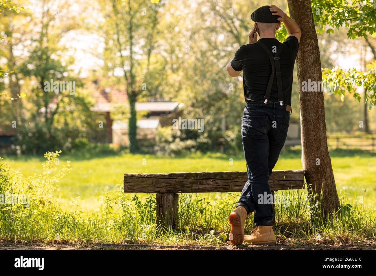 Un uomo che chiama con il suo telefono cellulare lavorando e facendo affari mentre si guarda su un campo di erba in una zona rurale in una giornata di sole durante la primavera Foto Stock