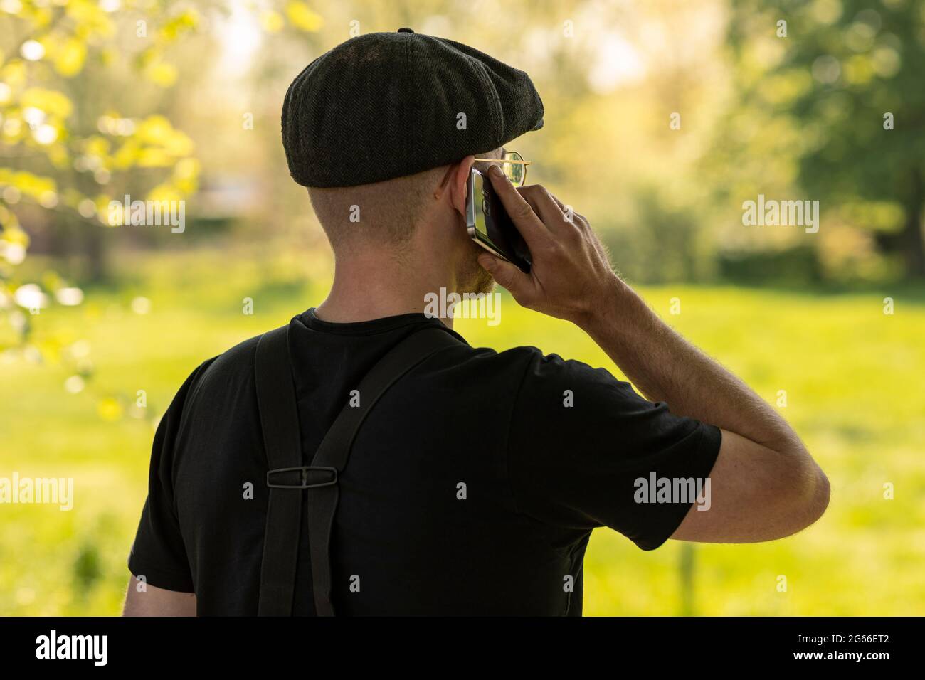 Un uomo contadino che indossa un berretto e vestiti casual che chiama con il suo telefono cellulare, lavorando e facendo affari mentre si guarda su un campo d'erba in un ar rurale Foto Stock