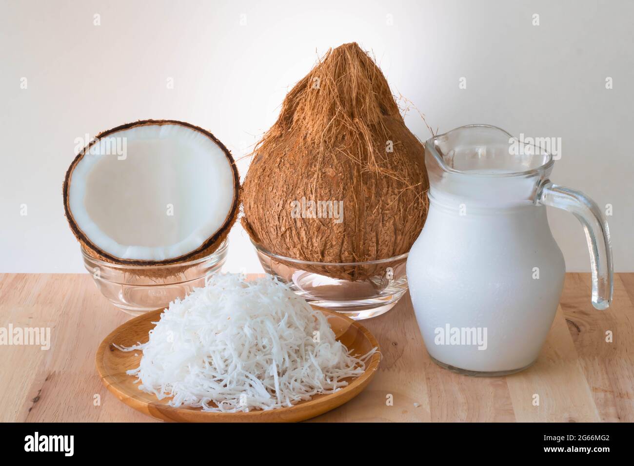 Prodotti di cocco, un intero cocco, mezzi, latte grattugiato e di cocco su tavolo di legno, sfondo bianco e spazio copia. Foto Stock