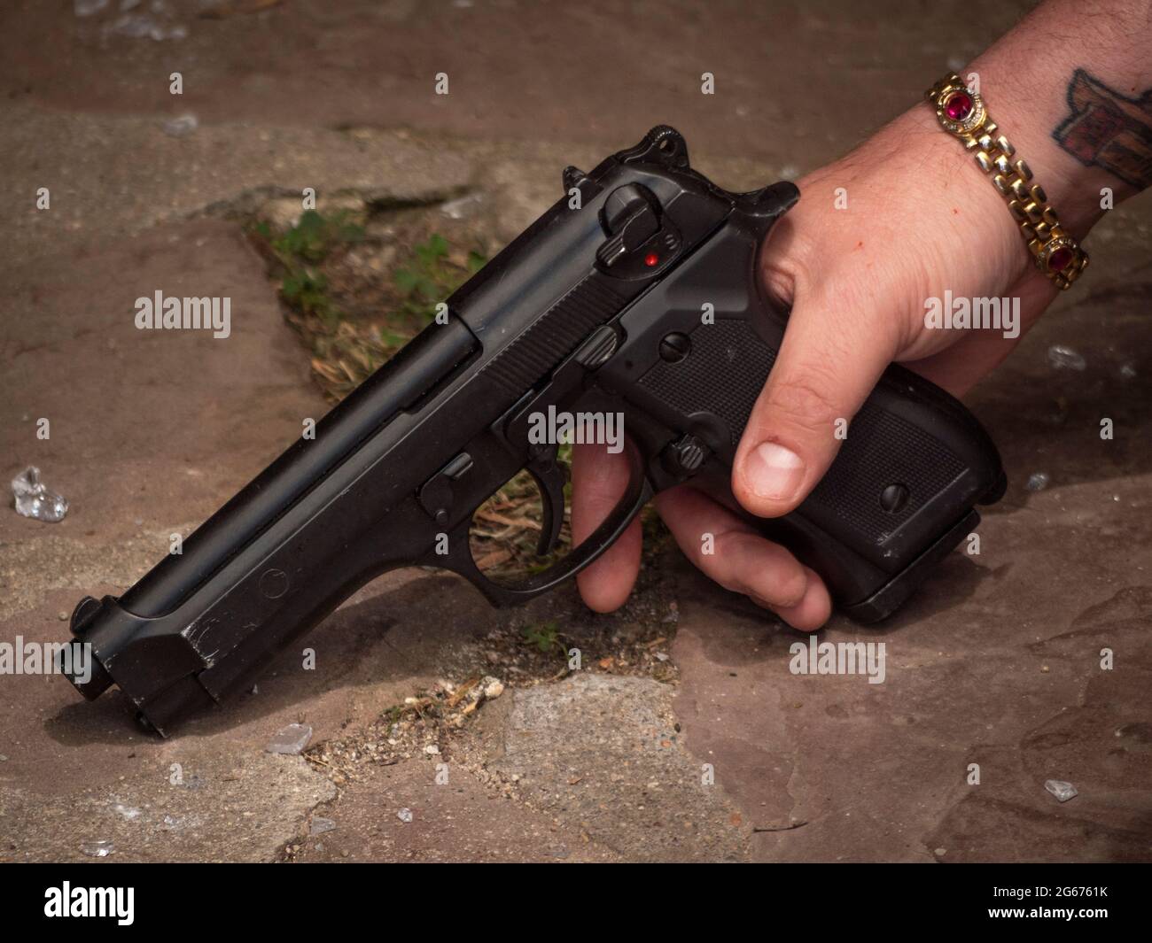 Primo piano ad angolo basso di 9mm pistola nelle mani di un membro della banda di abbigliamento militare. Foto Stock