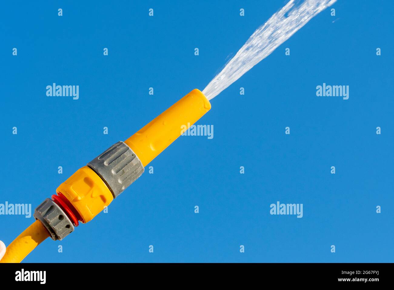 Spruzzatura di acqua da un tubo flessibile contro un cielo blu chiaro, Regno Unito. Foto Stock