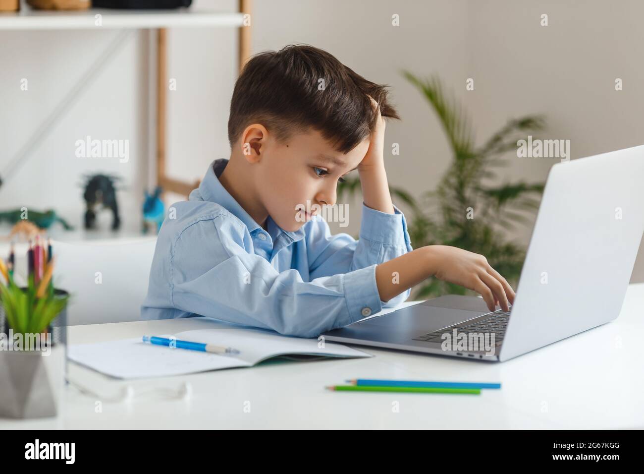 Bambino intelligente stanco di imparare compiti difficili utilizzando il computer portatile e Internet. E-learning scuola elementare tramite videochiamata. Ragazzo che studia online a casa Foto Stock