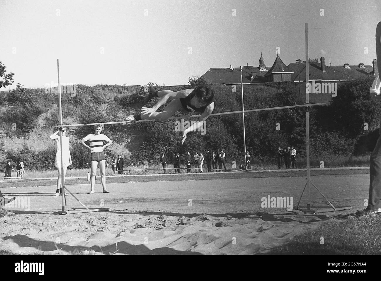1960s, storico, atletica, giornata sportiva inter-contea, giovane maschio concorrente che rotola il suo corpo sopra la barra nel salto alto, in procinto di atterrare nel pozzo di sabbia sotto, Inghilterra, Regno Unito. Foto Stock