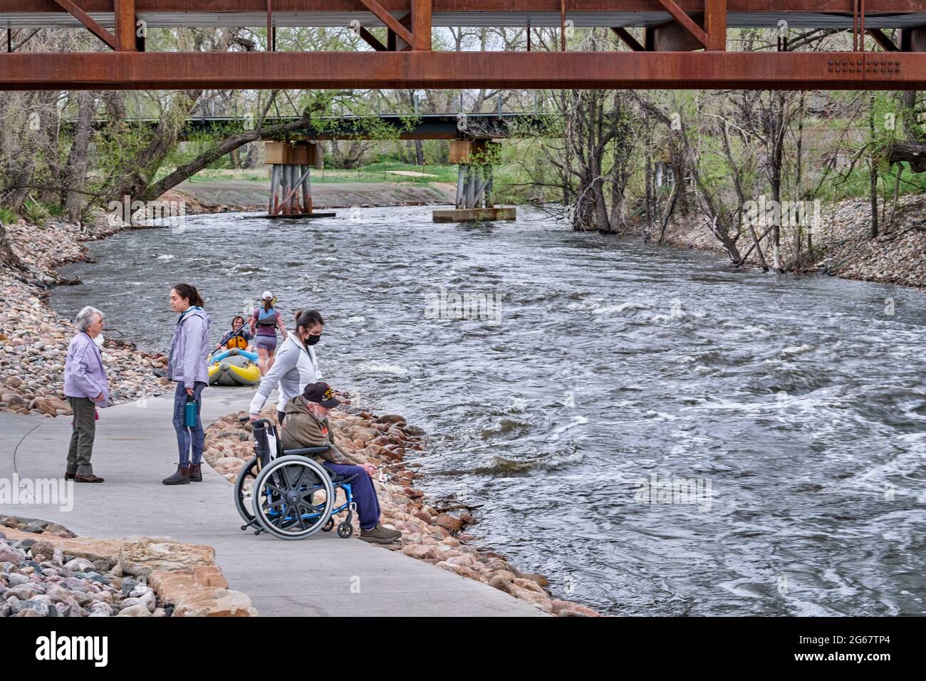 Fort Collins, CO, USA - 8 maggio 2021: Gruppo di persone con un uomo anziano in una sedia a rotelle che pesca sotto il Poudre River Whitewater Park, inizio primavera sc Foto Stock