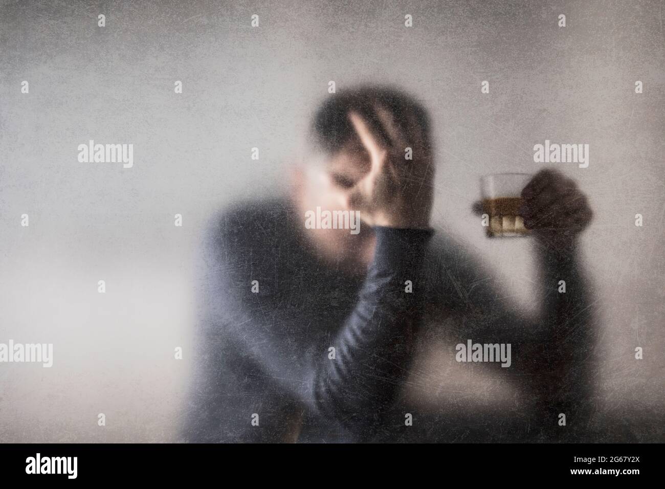 Uomo con un bicchiere di whisky dietro un vetro polveroso graffiato. Concetto di alcolismo. Foto Stock