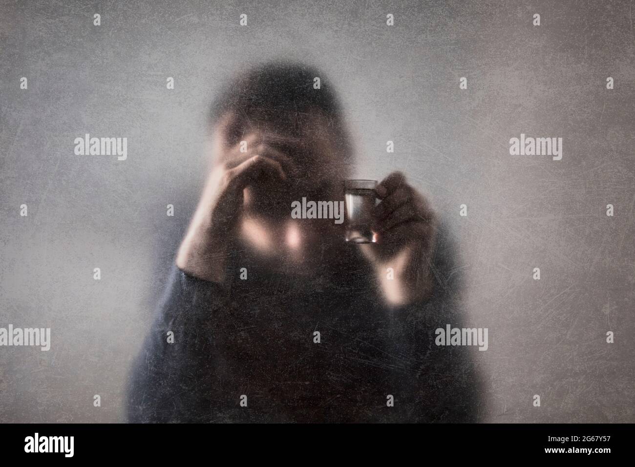 Uomo con un bicchiere di vodka dietro un vetro polveroso graffiato. Concetto di alcolismo. Foto Stock