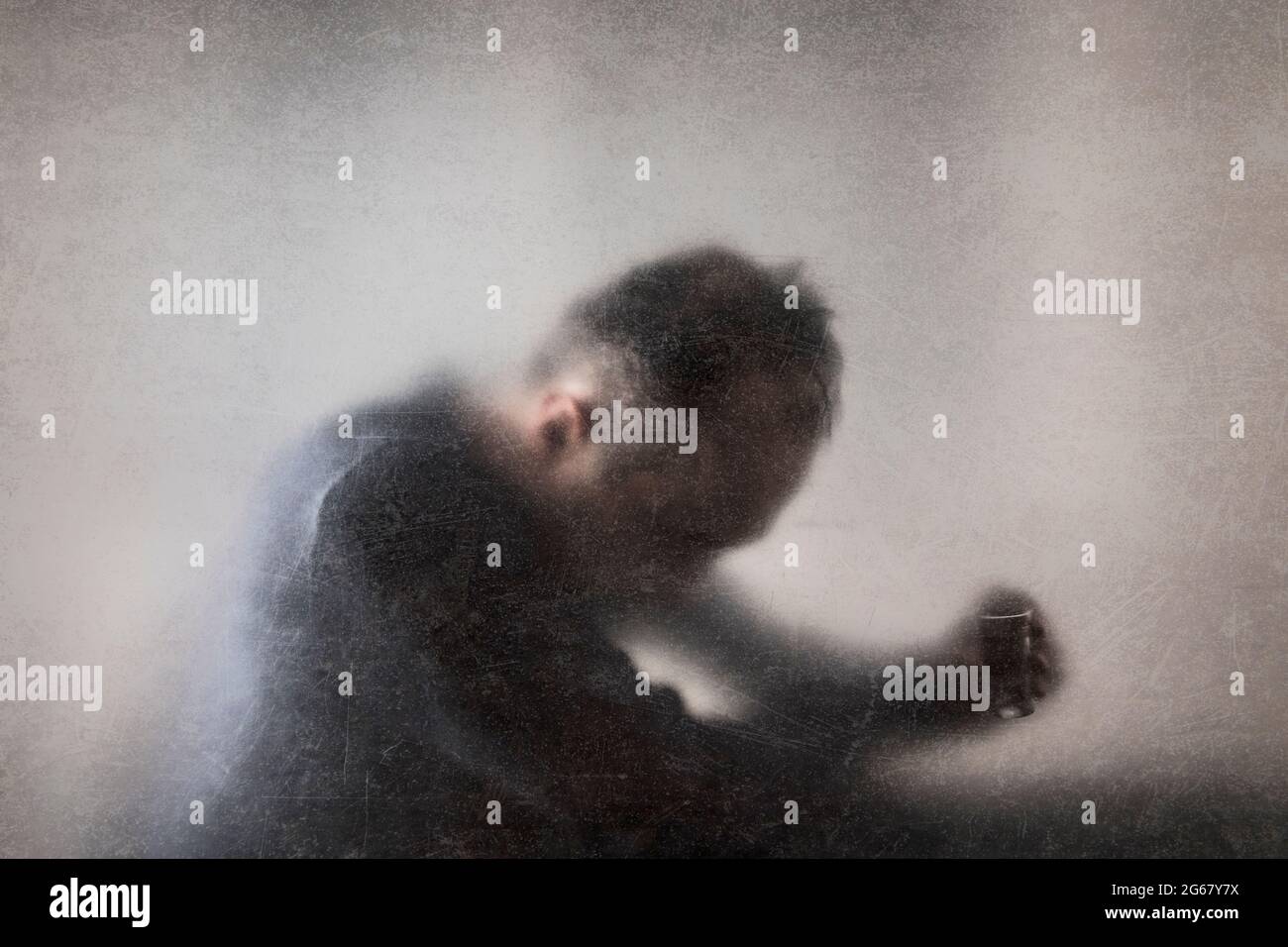 Uomo con un bicchiere di vodka dietro un vetro polveroso graffiato. Concetto di alcolismo. Foto Stock