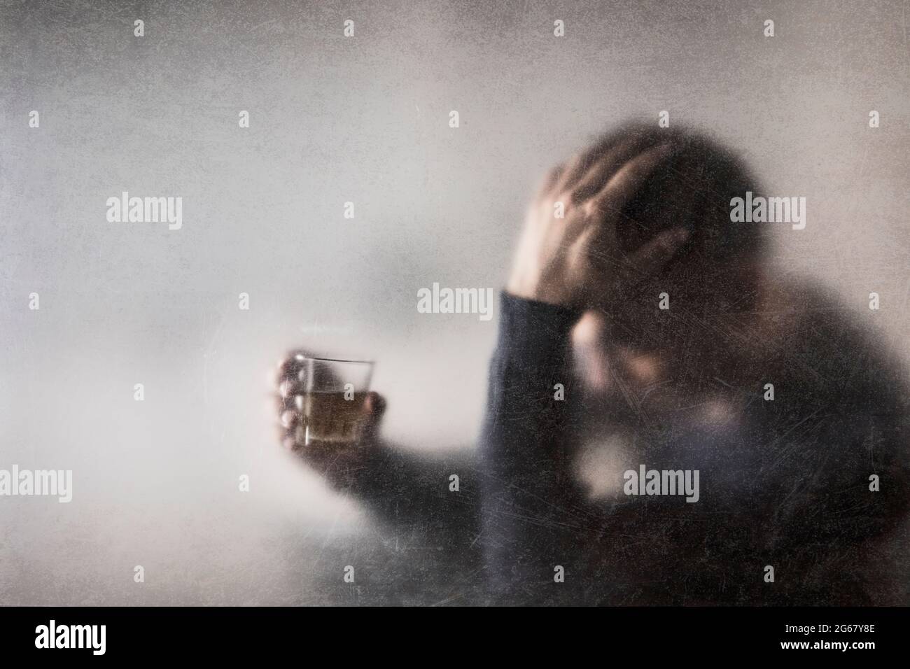 Uomo con un bicchiere di whisky dietro un vetro polveroso graffiato. Concetto di alcolismo. Foto Stock