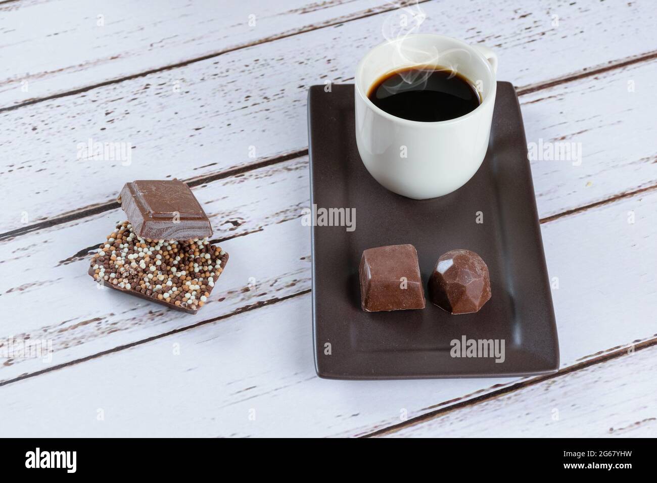 Barrette di cioccolato al latte con spruzzi, accanto a una tazza di caffè e caramelle di cioccolato fondente. Foto Stock