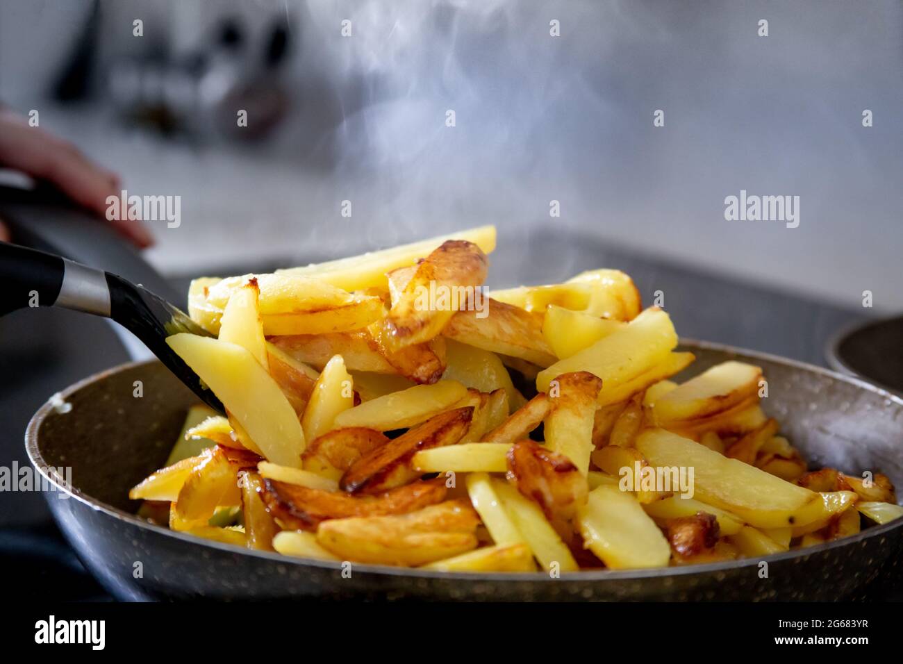 Primo piano di patate fritte con una crosta dorata in una padella, sono  visibili le mani del cuoco, che le sta mescolando con una spatola, vapore  sopra Foto stock - Alamy
