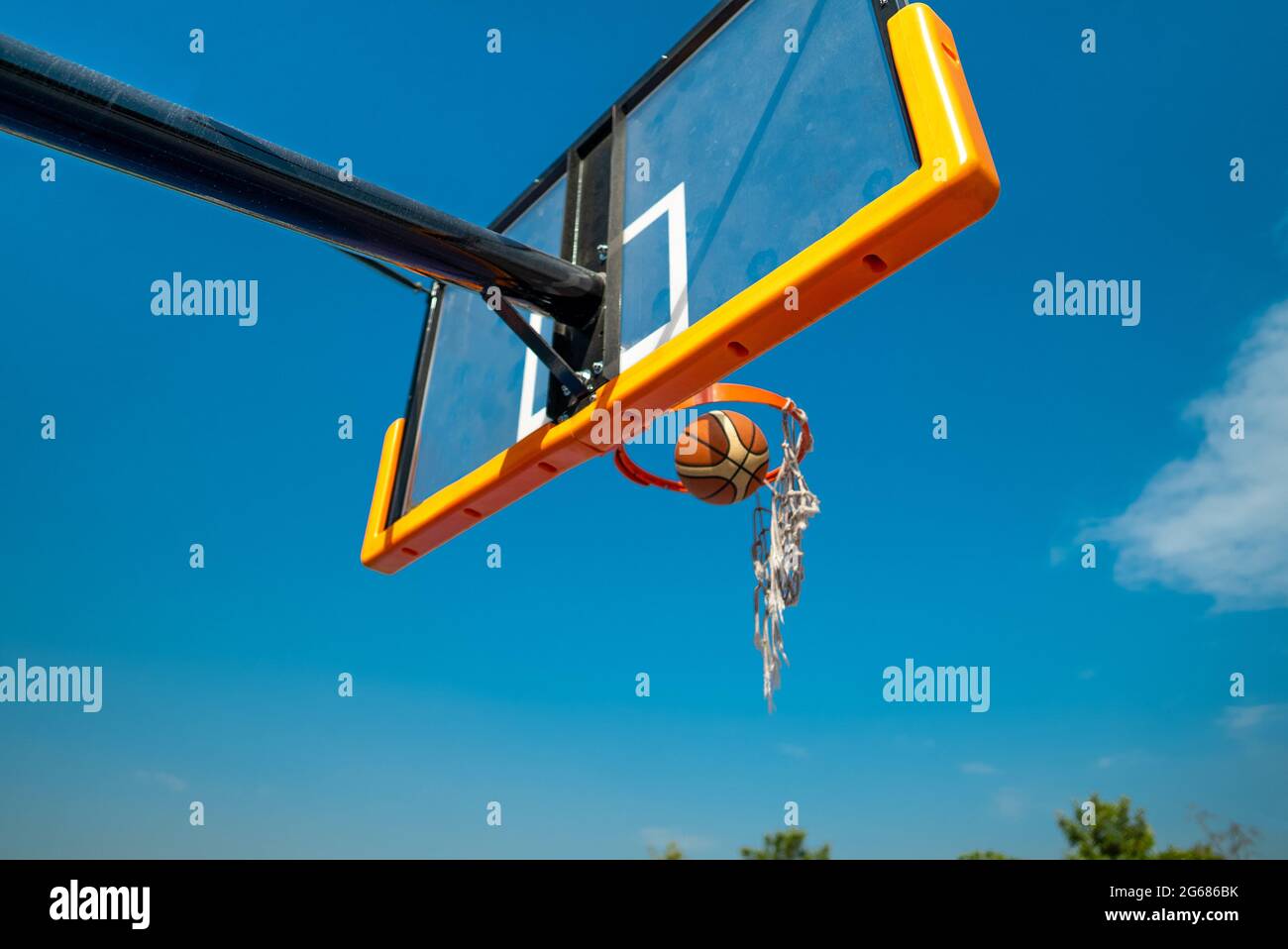 Palla di pallacanestro che cade attraverso rete rotta sul parco giochi dopo il colpo. Cielo blu su sfondo Foto Stock