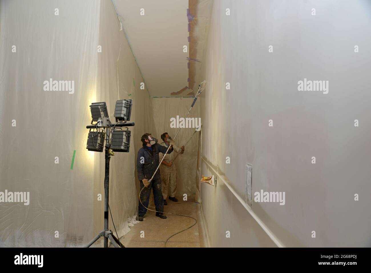 due artigiani utilizzano attrezzature spray senza aria per verniciare un rivestimento superiore sulle pareti di un edificio commerciale Foto Stock