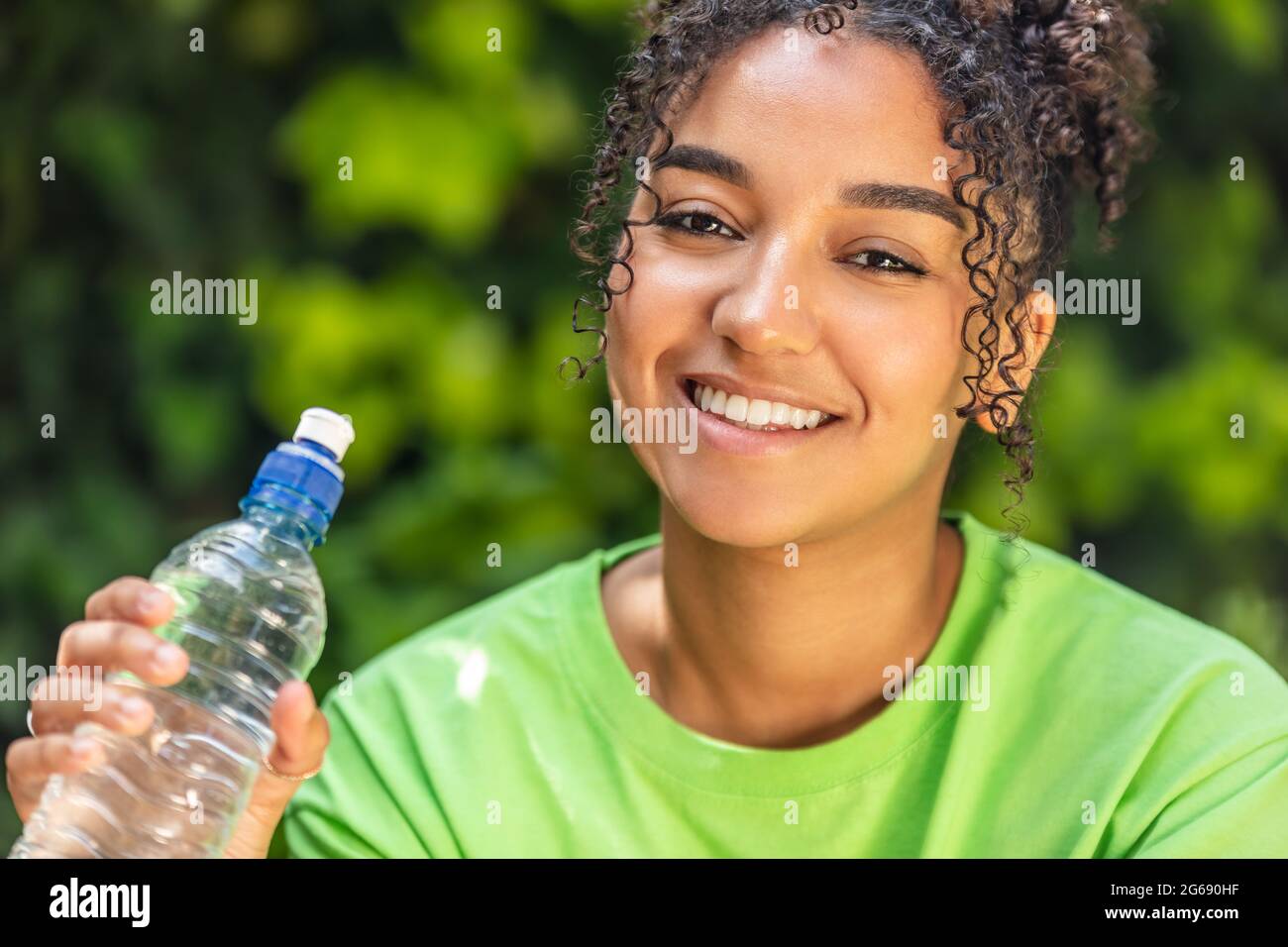 Ritratto all'aperto di bella felice gara mista Africana americana ragazza adolescente donna giovane con denti perfetti bere acqua da una bottiglia weari Foto Stock