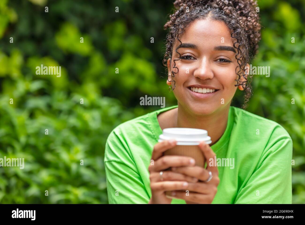 Bella felice mista razza Africana americana ragazza adolescente femmina giovane donna con denti perfetti sorridendo bere take away caffè o tè all'esterno Foto Stock