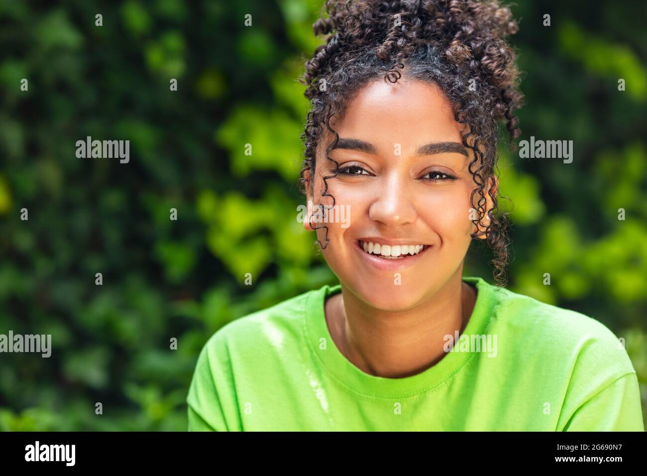 Ritratto all'aperto di bella felice gara mista biraciale afroamericana ragazza adolescente femmina giovane donna sorridente con denti perfetti indossando una t verde Foto Stock