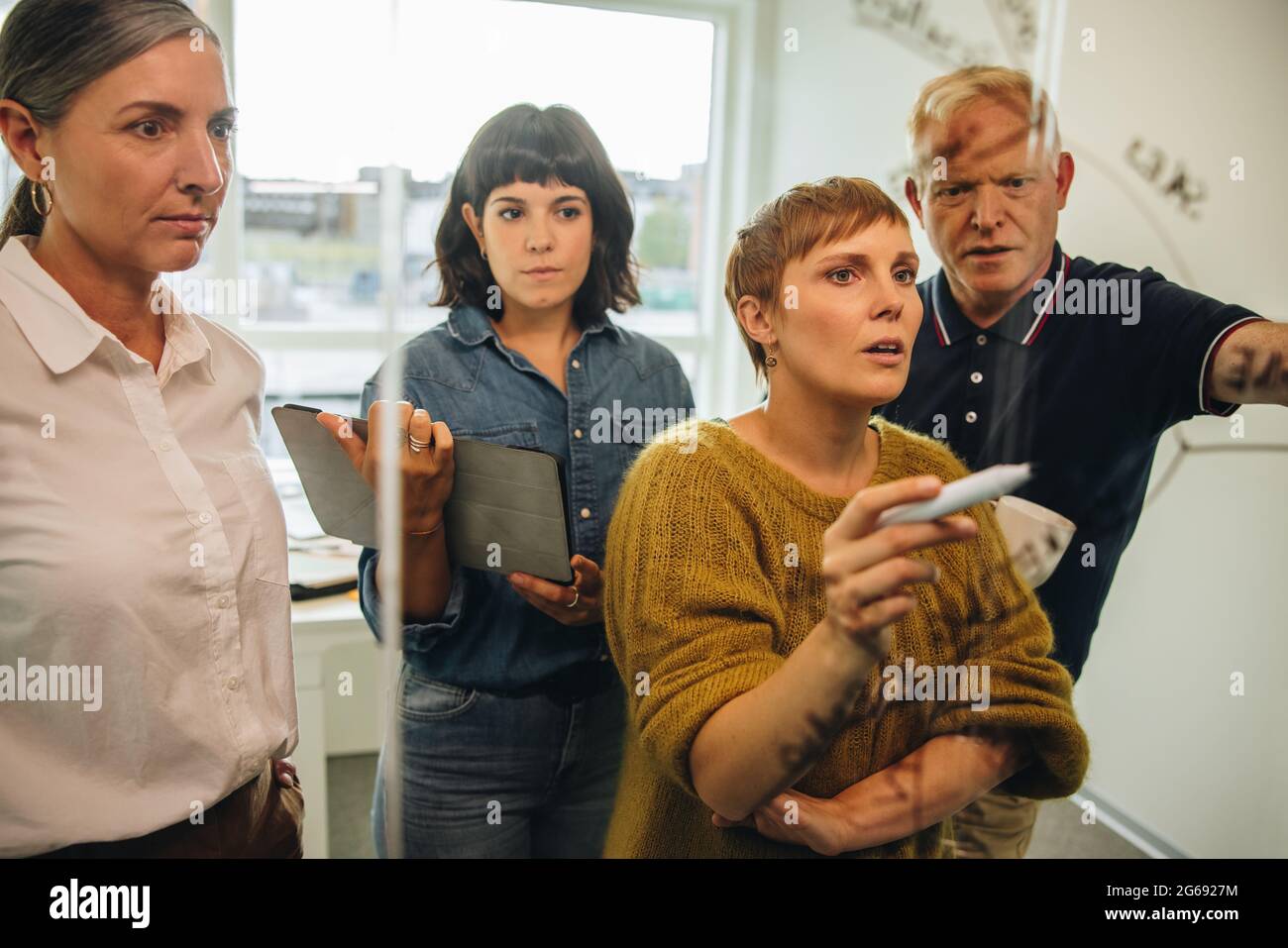 Dirigente donna in ufficio che scrive su una parete di vetro con colleghi in attesa. professionisti che discutono e scrivono su una parete di vetro durante una riunione Foto Stock