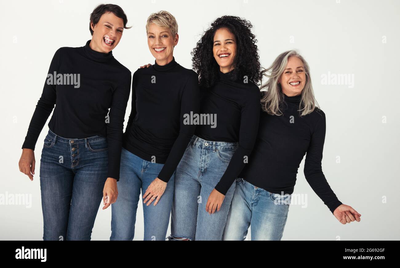 Gruppo stupefacente di donne diverse che celebrano la loro età in uno studio. Quattro donne positive del corpo di età differenti sorridenti allegro mentre indossa i jeans a. Foto Stock