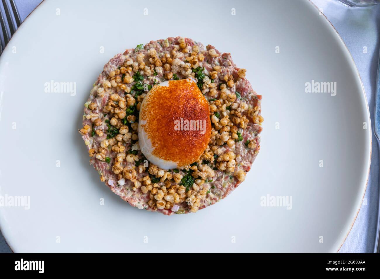 Tartare di bistecca, un piatto di carne di manzo crudo macinato, condito e servito con un uovo leggermente in camicia sopra su un piatto bianco Foto Stock