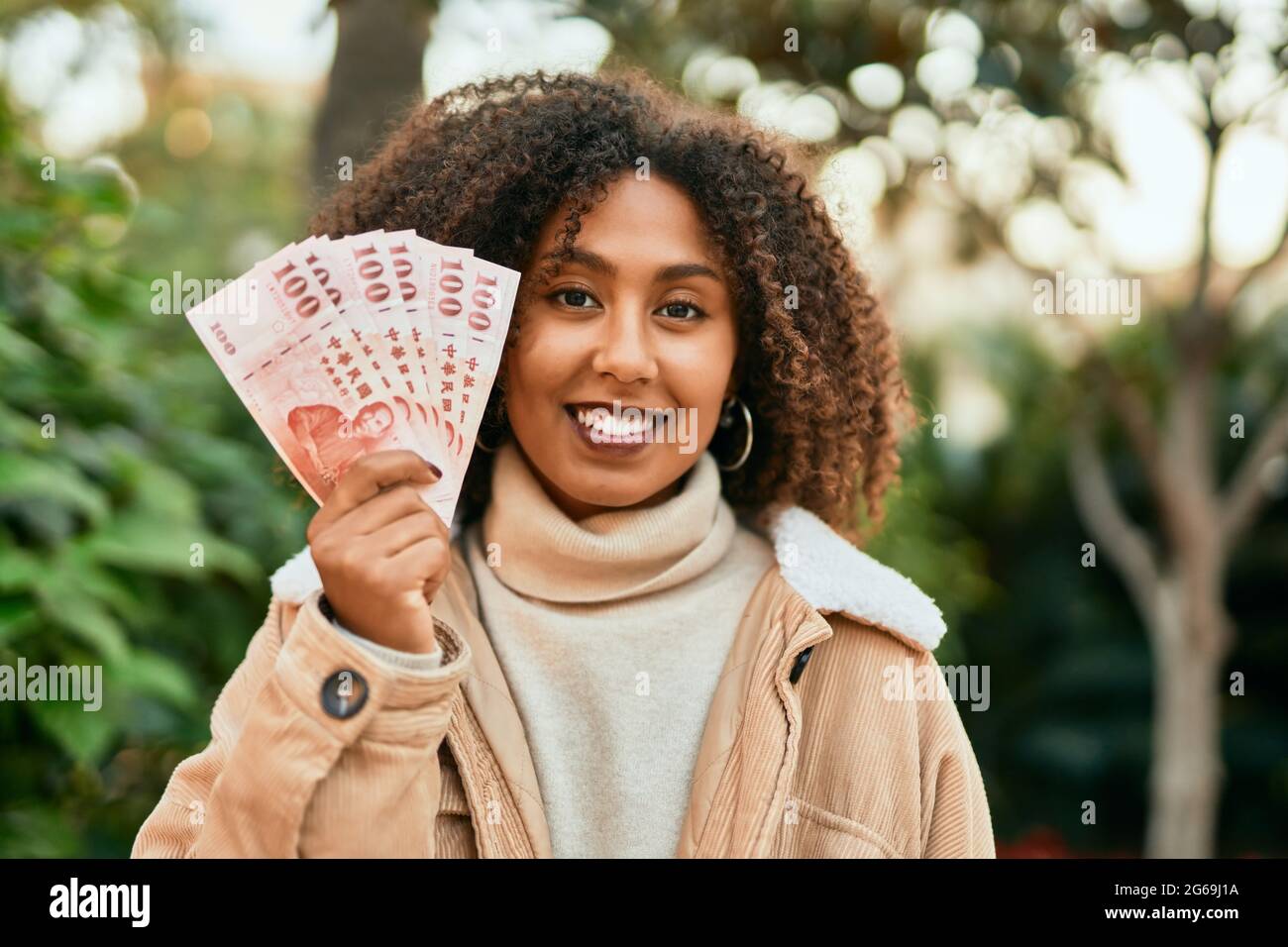 Giovane afroamericana sorridente felice di tenere nuovi dollari di taiwan al parco. Foto Stock