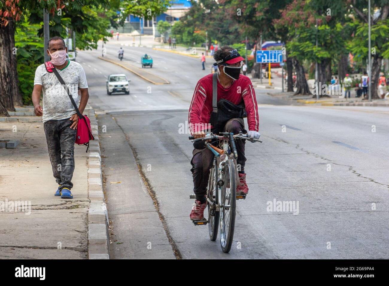 Uomo cubano in bicicletta in una strada cittadina a Santiago de Cuba, Cuba. Un altro cammina sul marciapiede. Entrambi indossano maschere facciali protettive come me Foto Stock