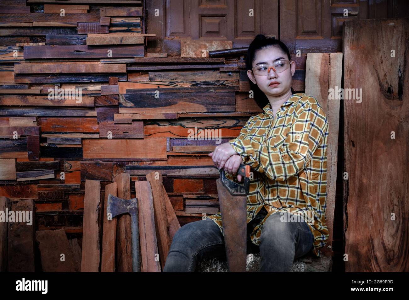 Donne carpentiere seduta con sega di presa a sfondo vecchio muro di legno Foto Stock