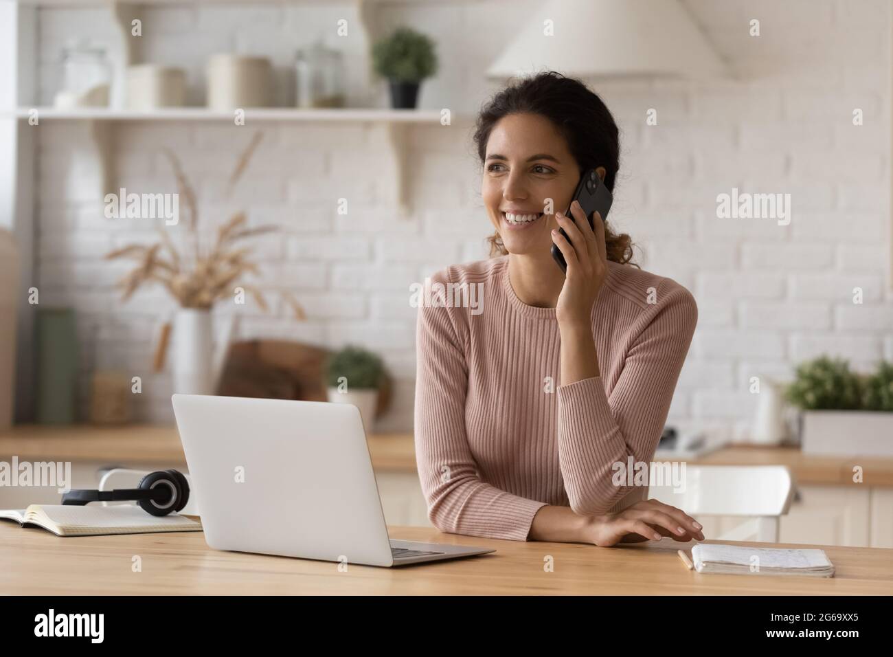 Felice giovane donna d'affari che tiene la conversazione del cellulare, lavorando sul computer. Foto Stock