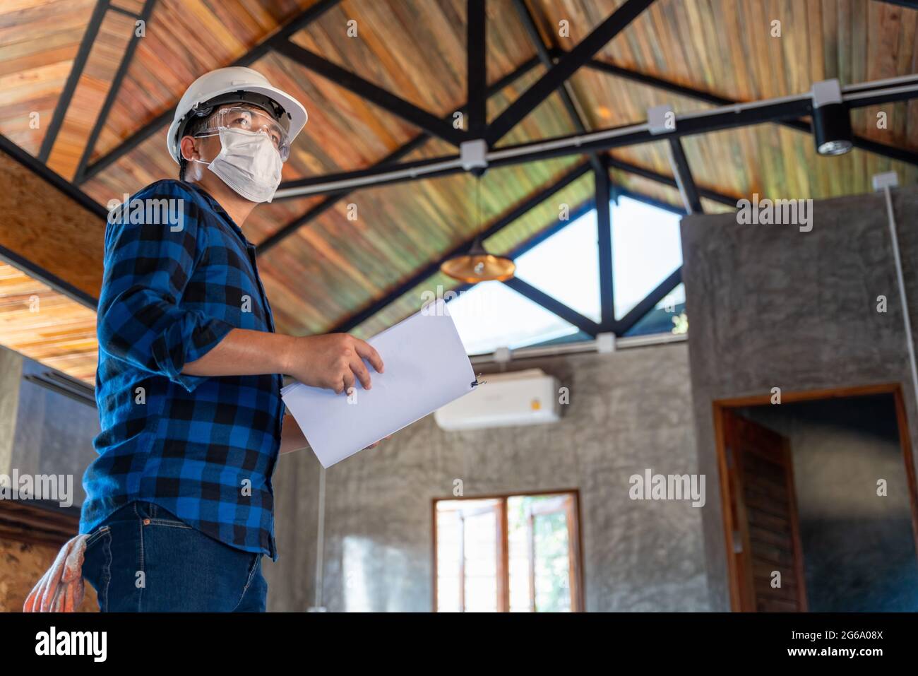 Ingegnere asiatico di costruzione tecnico ispezionare la struttura di legno sotto il tetto in cantiere o cantiere di una casa. Foto Stock