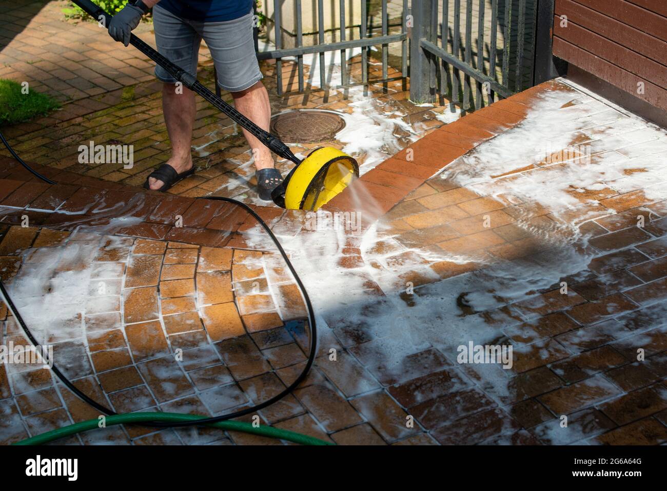 Uomo che pulisce le piastrelle di pavimentazione del cortile con idropulitrice ad alta pressione. Messa a fuoco selettiva. Foto Stock