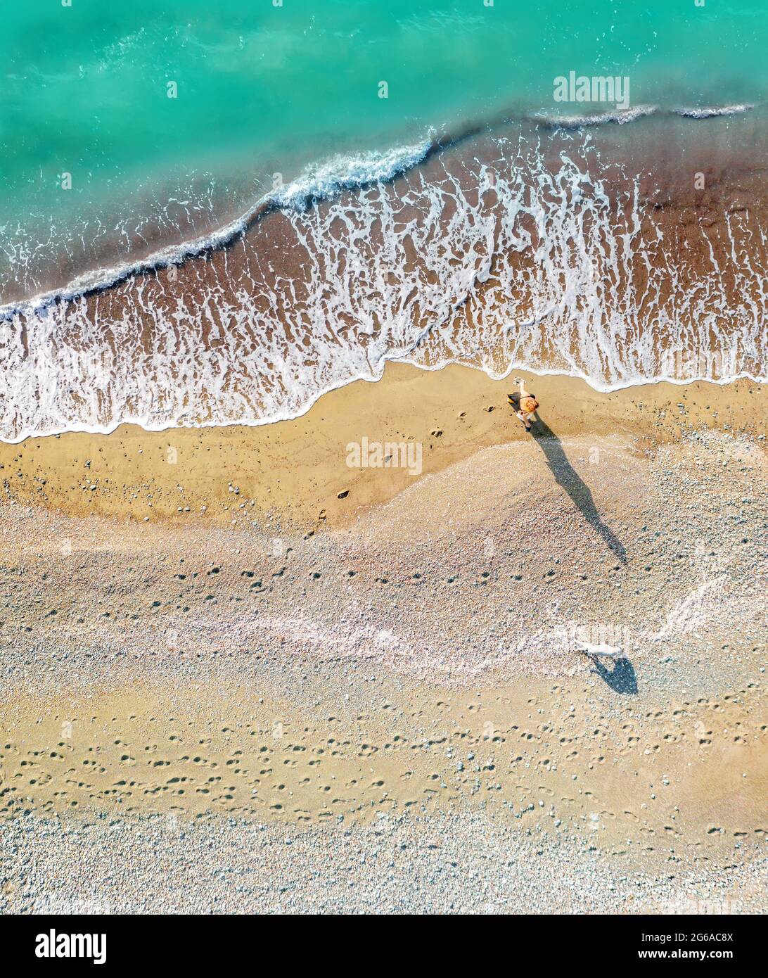 Una donna e un cane che camminano lungo la riva del mare lasciando impronte sulla sabbia, tiro aereo verticale direttamente sopra Foto Stock